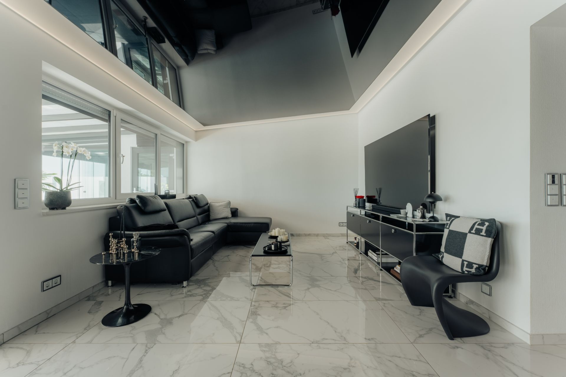 Modernes Wohnzimmer mit schwarzem Sofa, Flachbildfernseher und Marmorboden.