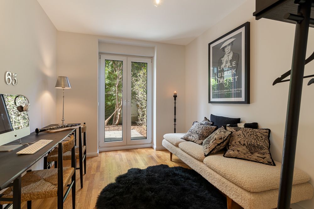 Helles Zimmer mit Sofa, Schreibtisch, Computer und Glastür zum Garten.