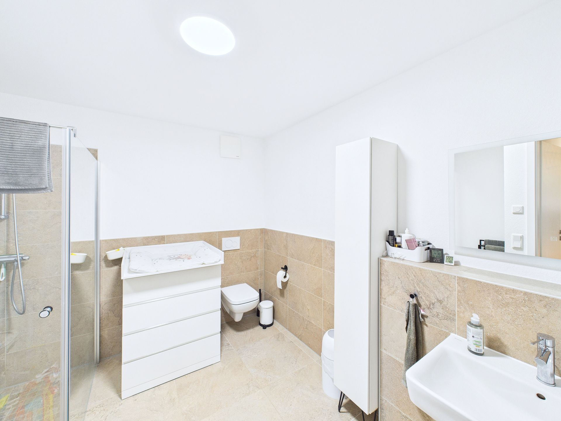 Modernes Badezimmer mit Dusche, Waschbecken, Toilette und weißen Badmöbeln.
