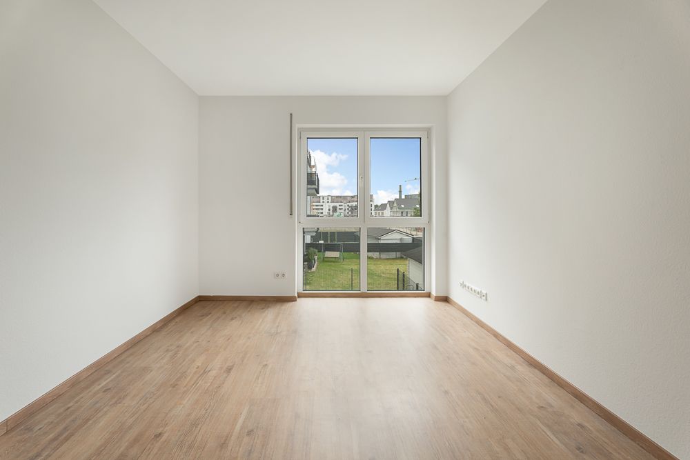 Leerer Raum mit Holzfußboden und großem Fenster mit Blick ins Grüne.