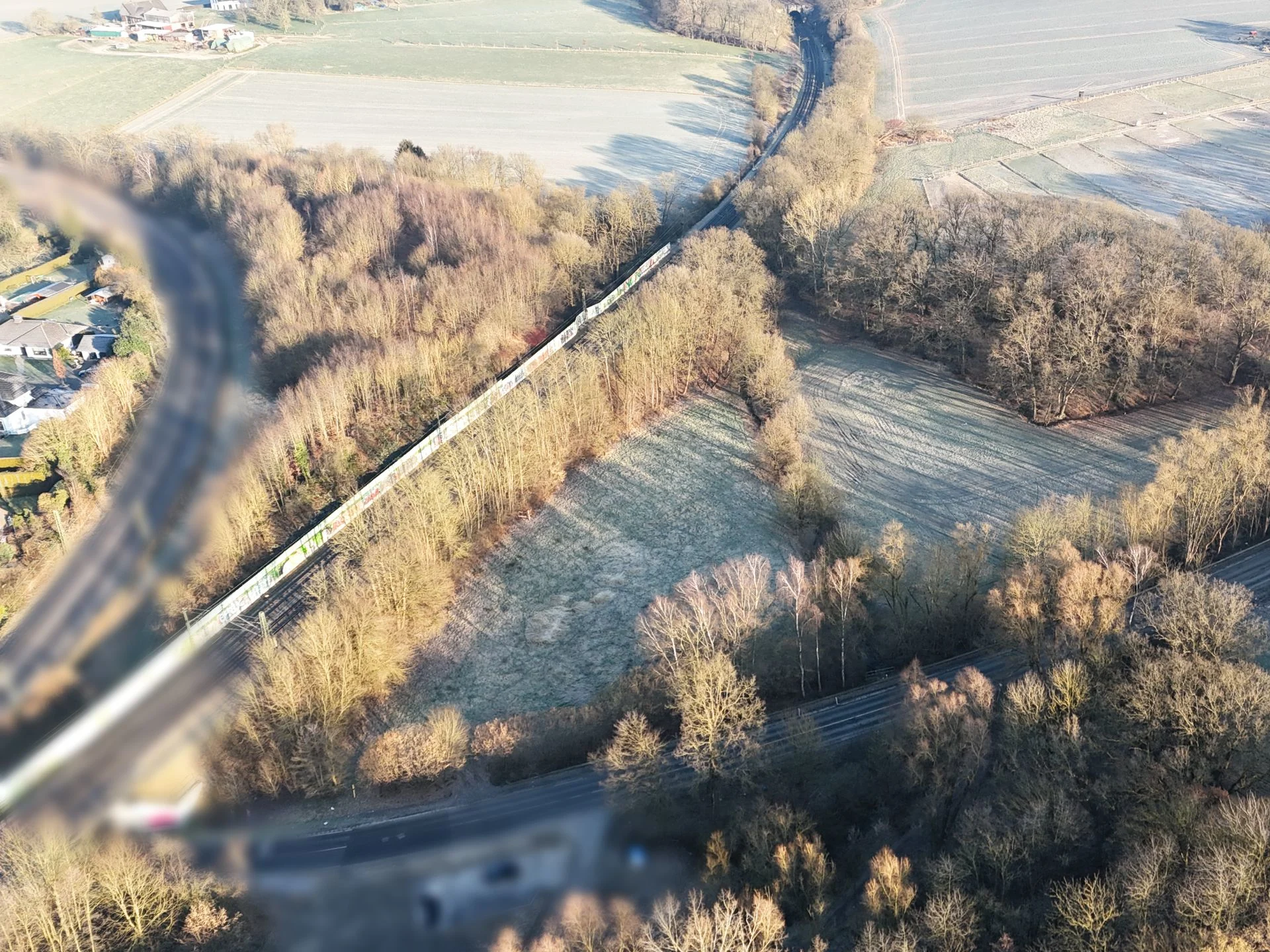 Luftaufnahme von Feldern, Wäldern und einer Bahnlinie, die durch die Landschaft verläuft.