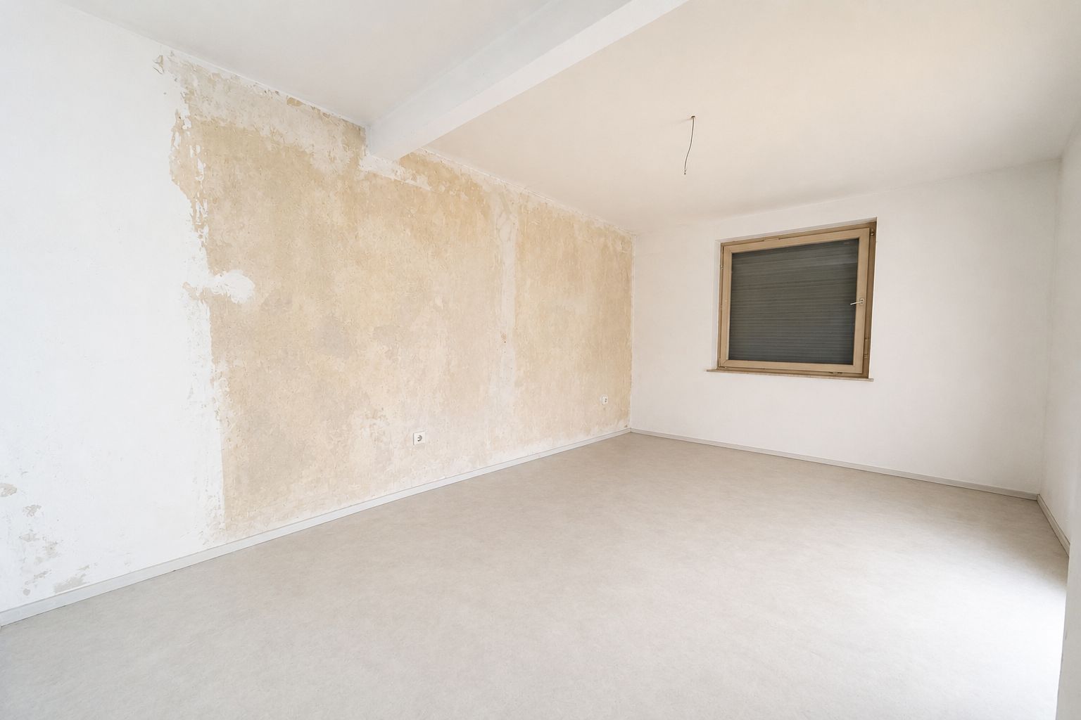 Leerer Raum mit teilweise abgeblätterter Wand und geschlossenem Fenster.