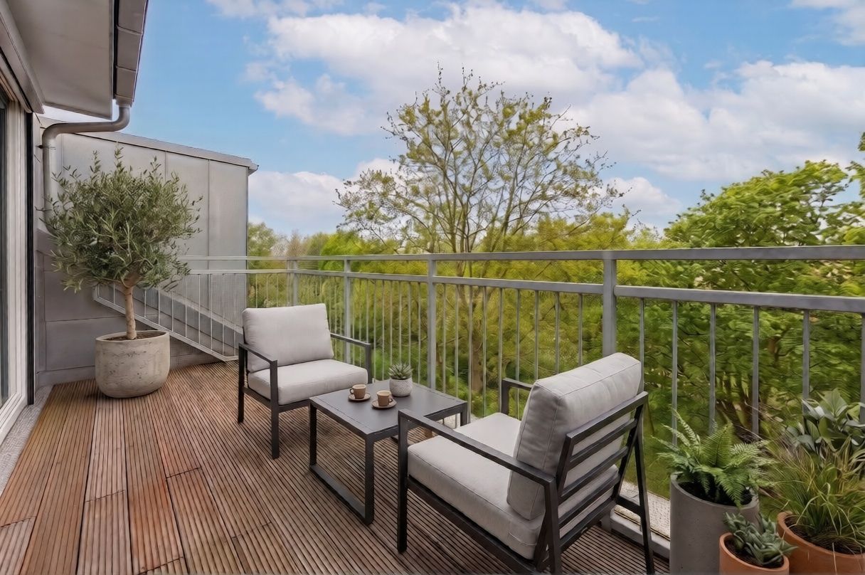 Balkon mit zwei Stühlen, Tisch, Pflanzen und Blick auf grüne Bäume.