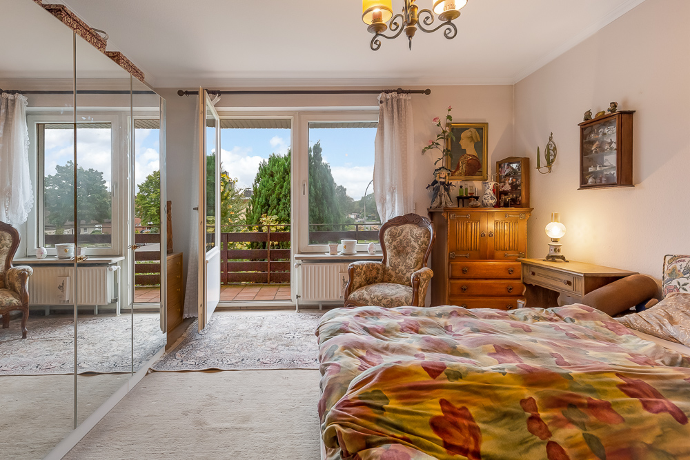Helles Schlafzimmer mit Doppelbett, Spiegel-Schrank, Balkon und klassischen Möbeln.