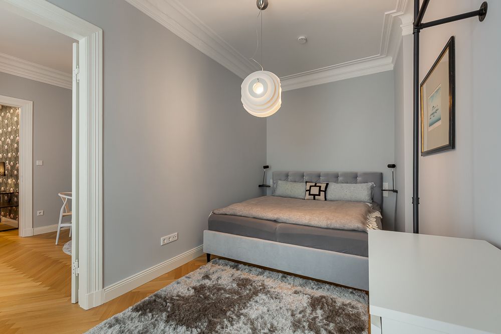 Helles Schlafzimmer mit Doppelbett, grauem Teppich, weißer Kommode und moderner Hängelampe.