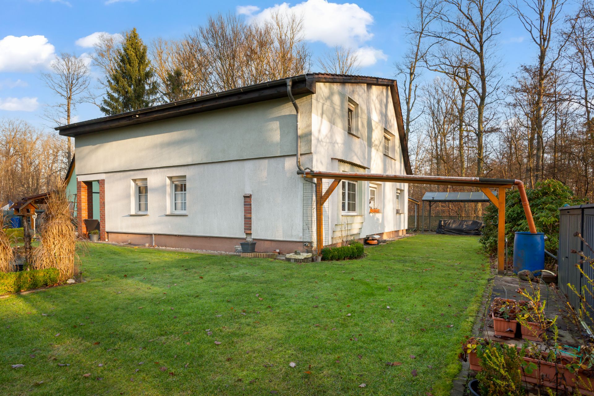 Zweistöckiges Wohnhaus mit weißer Fassade im Garten, umgeben von Bäumen und Rasen.