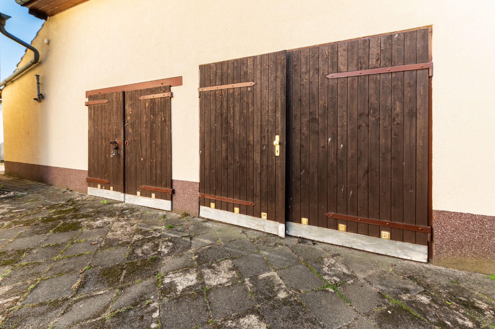 Drei braune Holztüren an einer Hauswand auf gepflastertem Boden.