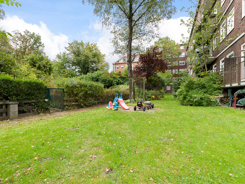 Grüner Garten mit Rutsche, Spielzeugauto und Baum neben Wohngebäude.