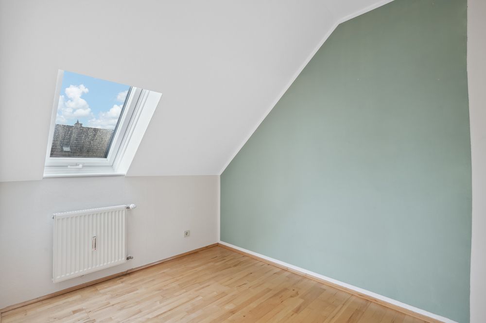 Heller Raum mit schräger Decke, Dachfenster, Heizkörper und grün gestrichener Wand.