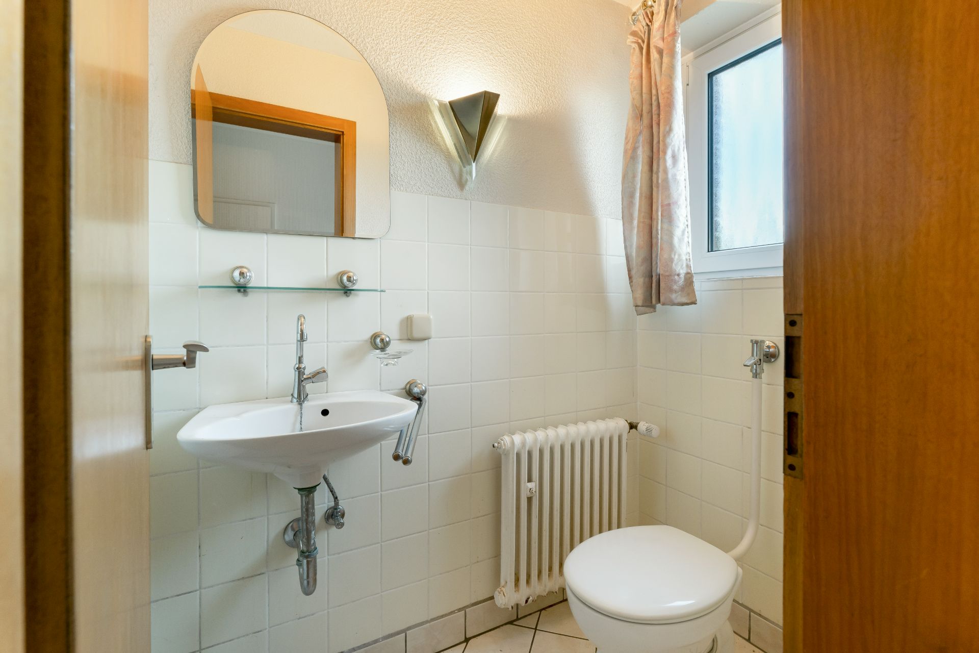 Kleines Badezimmer mit Waschbecken, Spiegel, Heizung, Toilette und Fenster.