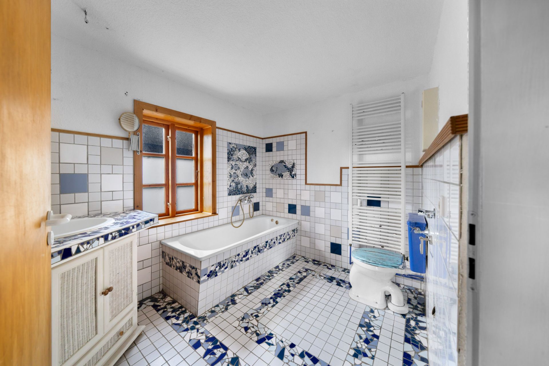 Badezimmer mit Badewanne, Fenster, Toilette und gemusterten Fliesen.