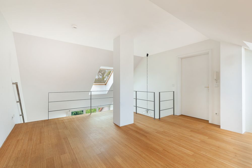 Heller Raum mit Holzfußboden, weißem Geländer und einem Dachfenster.