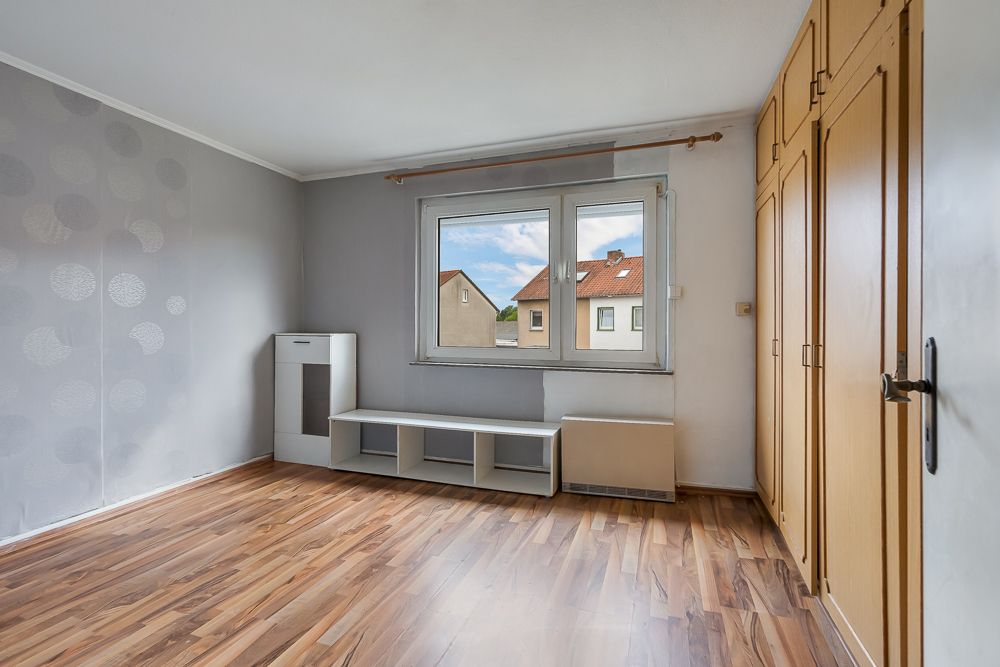 Leeres Zimmer mit Holzfußboden, großem Fenster, Einbauschrank und niedrigem Regal.