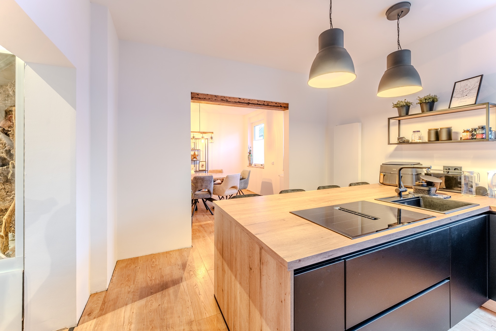 Moderne Küche mit Holzinsel, Kochfeld, Spüle und Blick ins Esszimmer mit Stühlen.