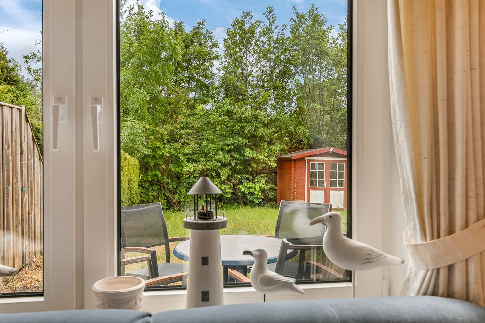 Blick durch ein Fenster auf Garten mit Sitzgruppe und rotem Gartenschuppen.