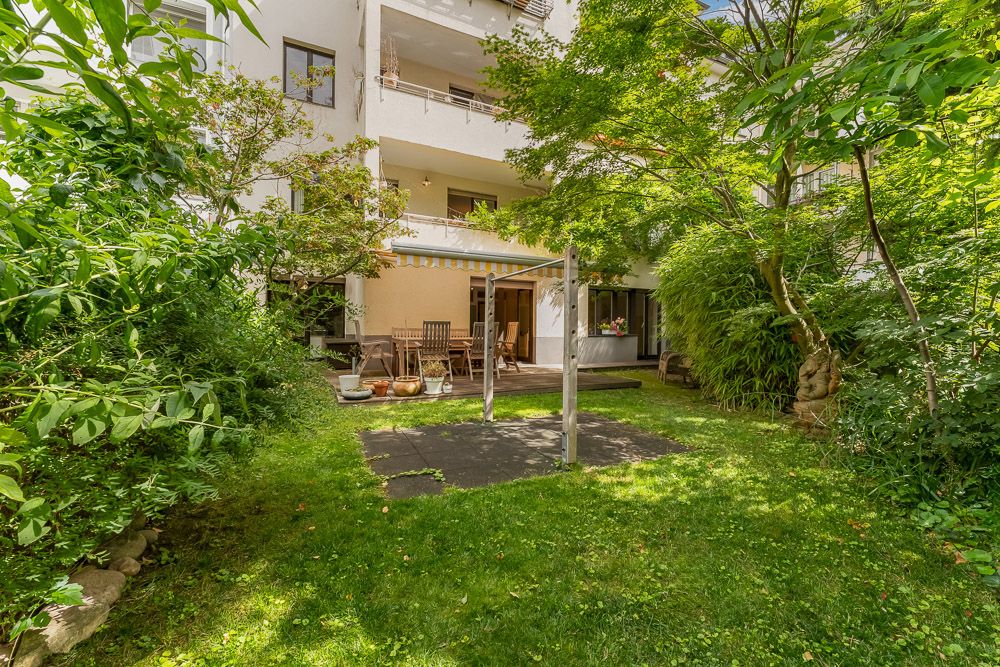 Grüner Garten mit Terrasse, Sitzmöbeln und Wäscheleine vor einem Wohnhaus.