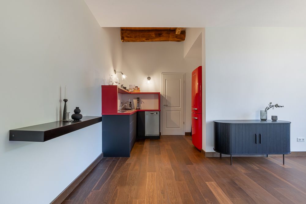 Moderne Küche mit rotem Kühlschrank, Holzboden und minimalistischer Dekoration.