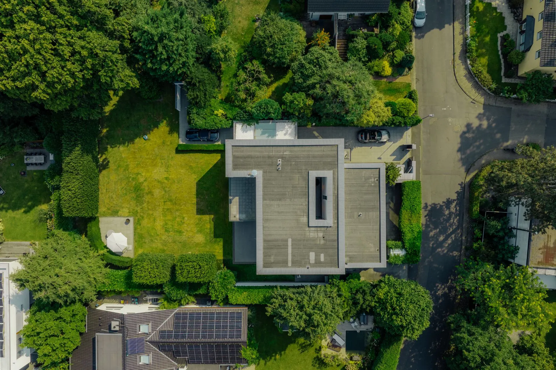 Luftaufnahme eines modernen Hauses mit großem Garten und umliegender Straße.