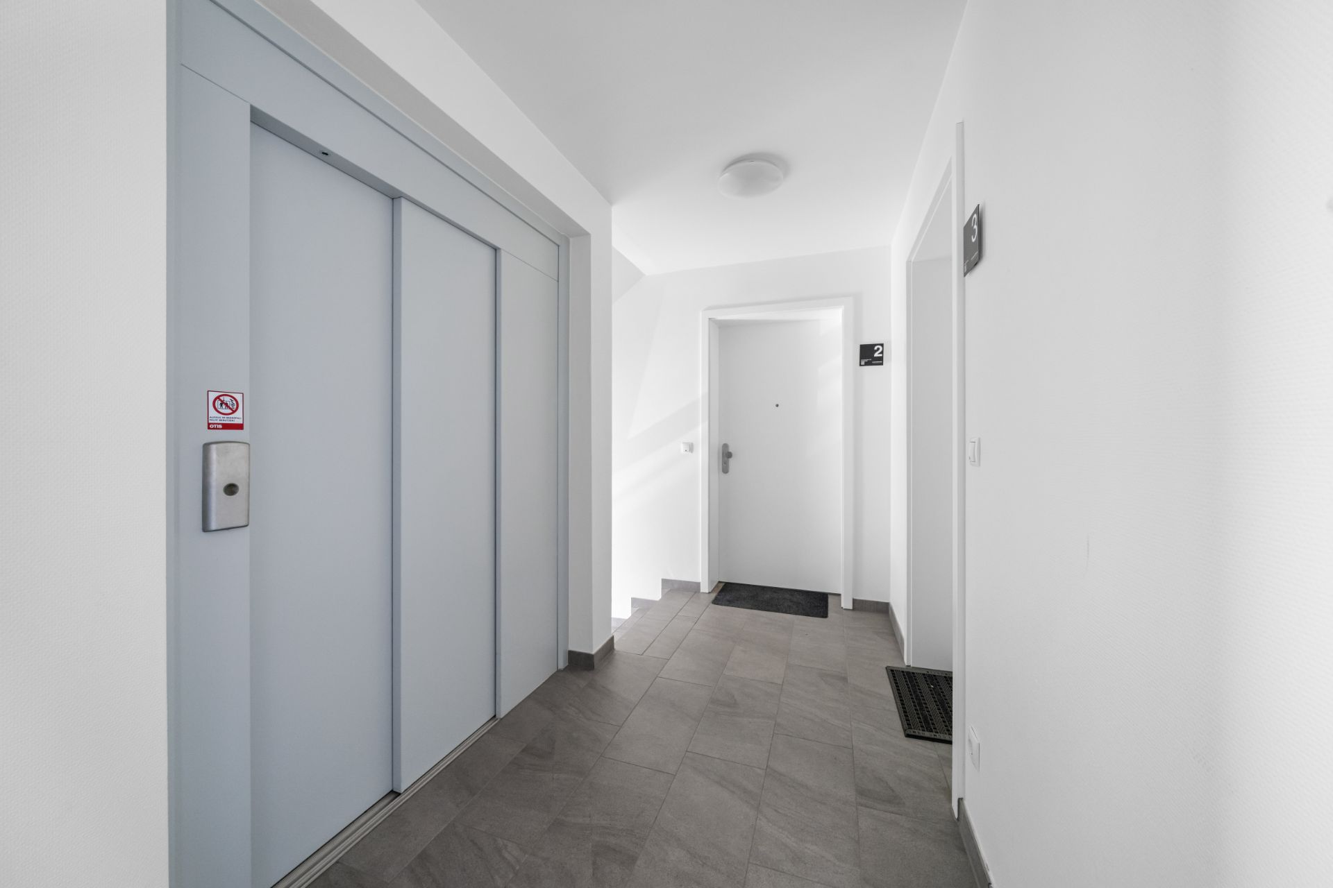 Heller Flur mit Aufzug und mehreren Wohnungstüren in einem Wohnhaus.