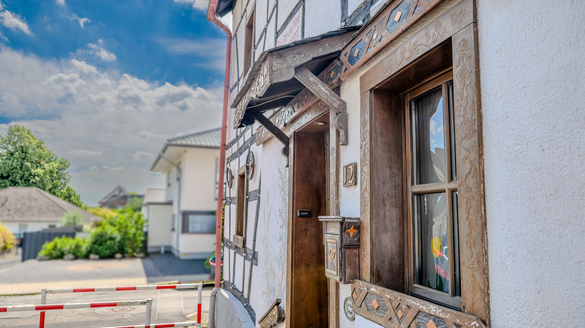 Eine Hausfassade mit Fachwerkelementen, Holztür, Fenster und Hausnummer 12 an einer ruhigen Straße.