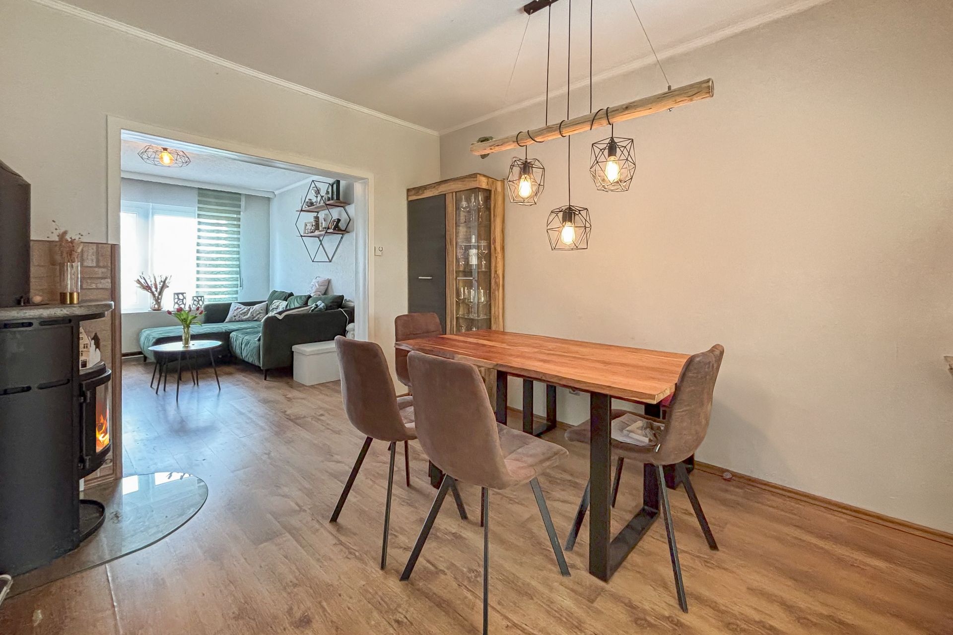 Essbereich mit Holztisch, fünf Stühlen, Hängelampen und Blick ins Wohnzimmer mit Sofa.