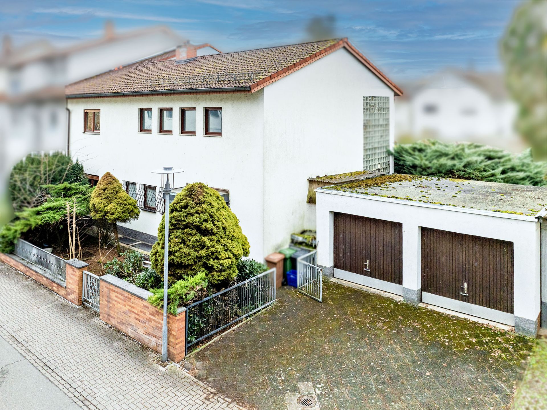 Zweistöckiges Wohnhaus mit Garten, Zaun, Doppelgarage und gepflasterten Hof.