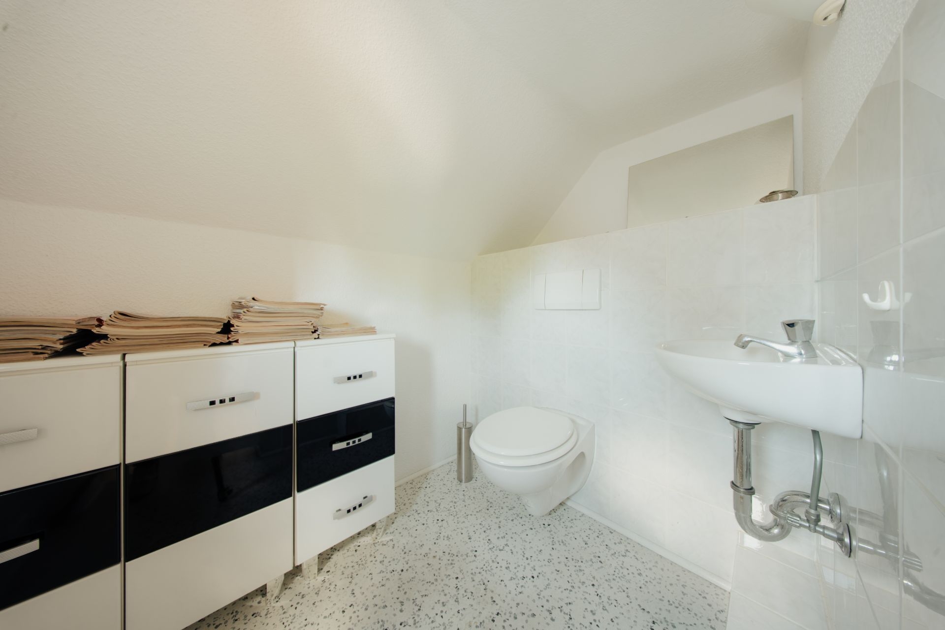 Kleines Badezimmer mit Wandtoilette, Waschbecken und weißem Schrank auf gemustertem Boden.