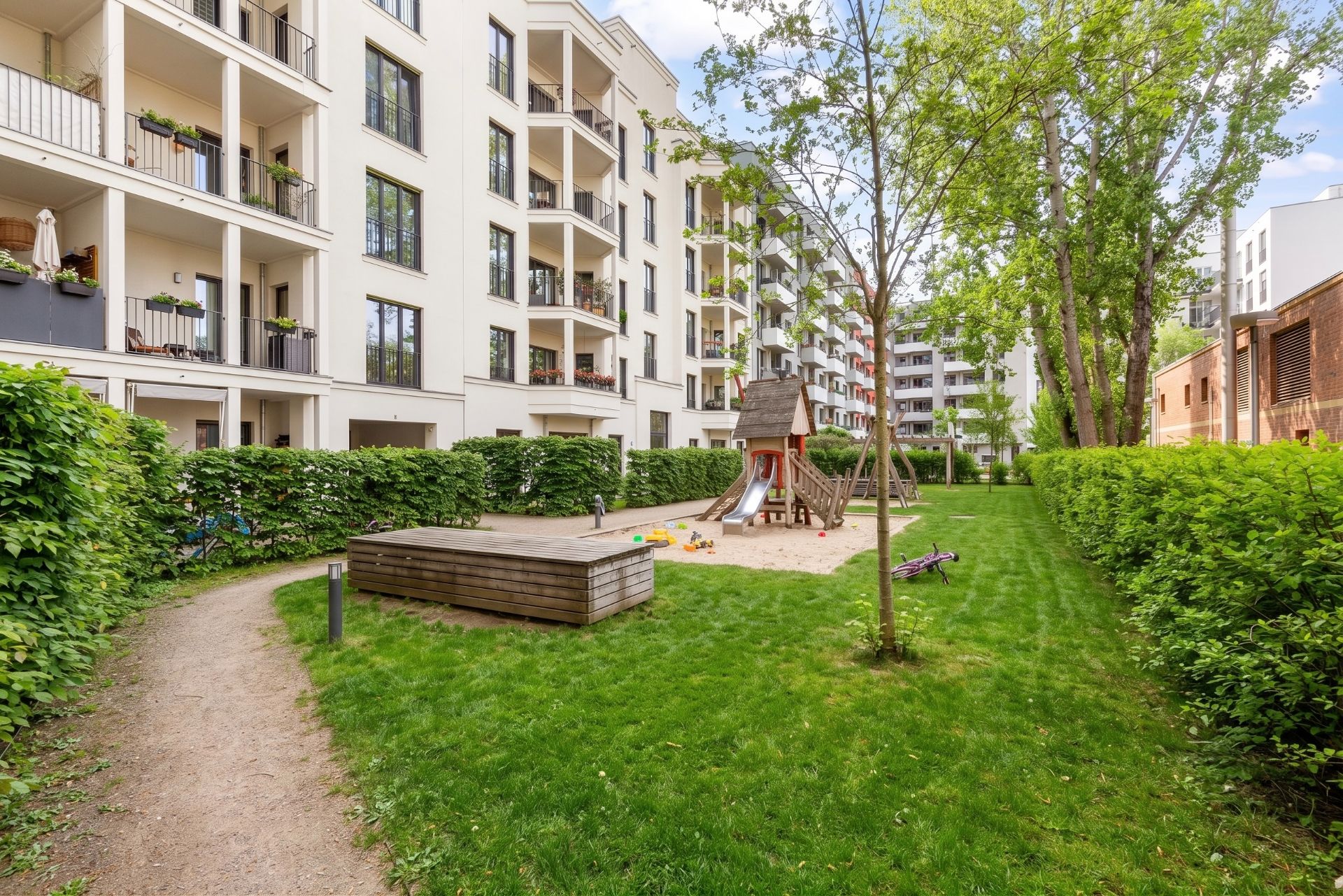 Grüner Innenhof mit Spielplatz und Sandkasten bei einem modernen Wohnhaus.