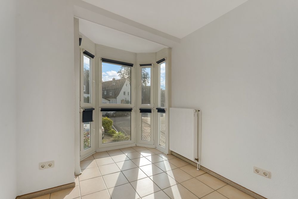 Heller Raum mit Fliesenboden, Eckfensterfront und Heizkörper an der Wand.