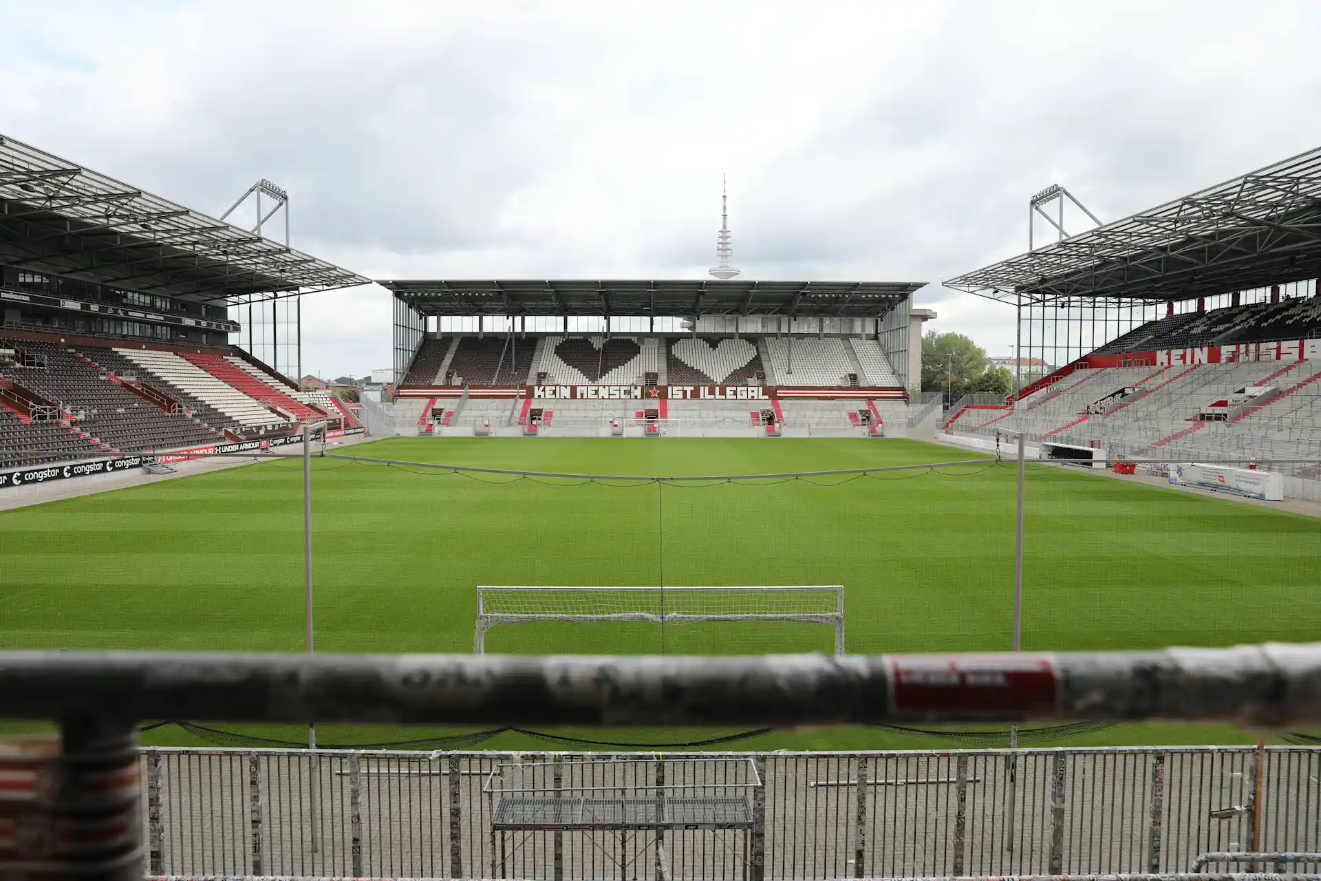 Leeres Fußballstadion mit grünem Rasen und leeren Tribünen, mittig ein Tor.