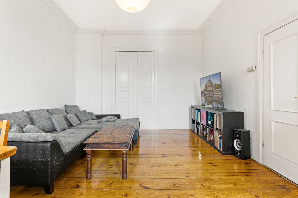 Wohnzimmer mit grauem Sofa, Holztisch, TV und Bücherregal auf Holzfußboden.