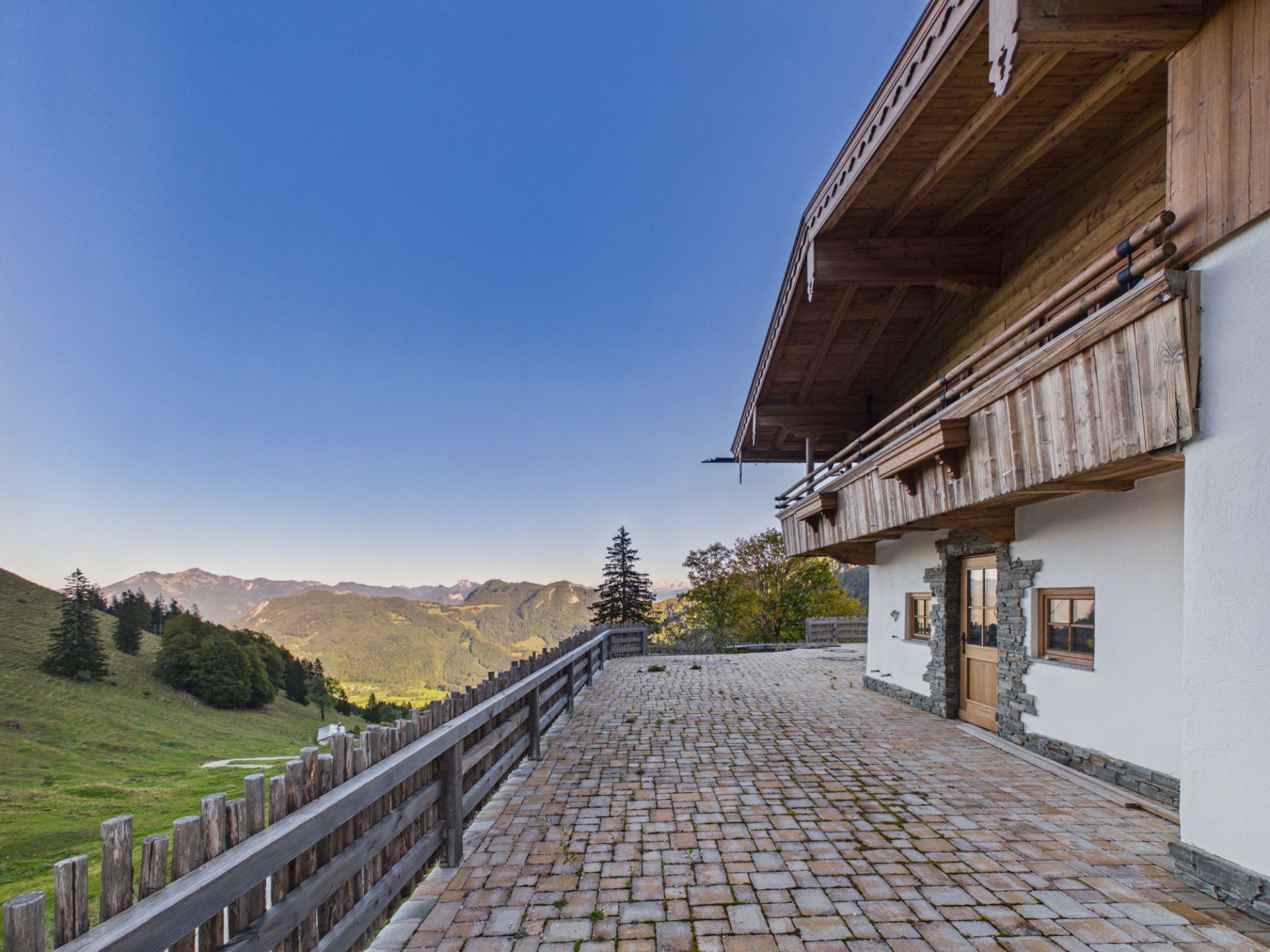 Große Terrasse mit Pflastersteinen an einem Haus in den Bergen, mit weitem Blick auf grüne Hügel.