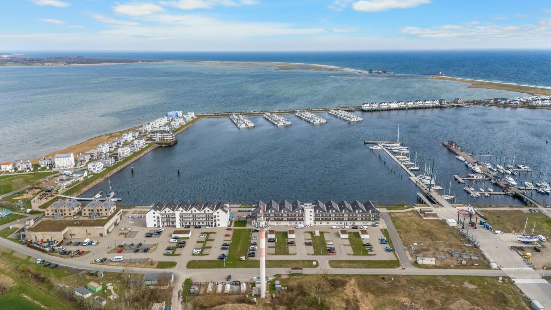 Luftaufnahme eines Yachthafens mit Wohngebäuden und parkenden Autos am Wasser.