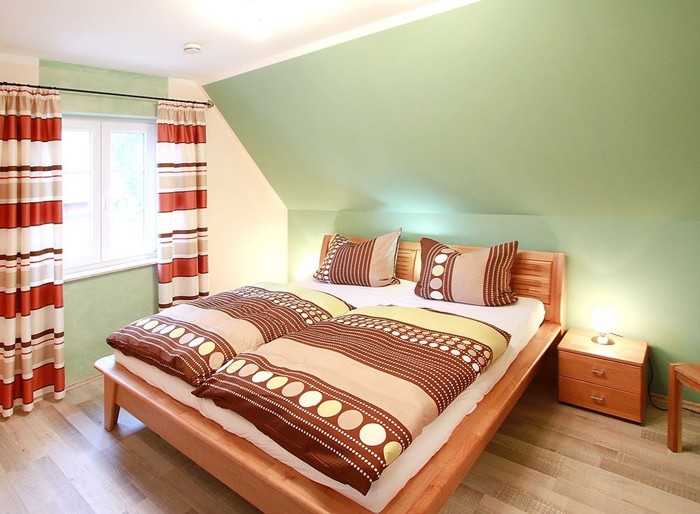 Helles Schlafzimmer mit Doppelbett, Nachttischen und Fenster mit gestreiften Vorhängen.