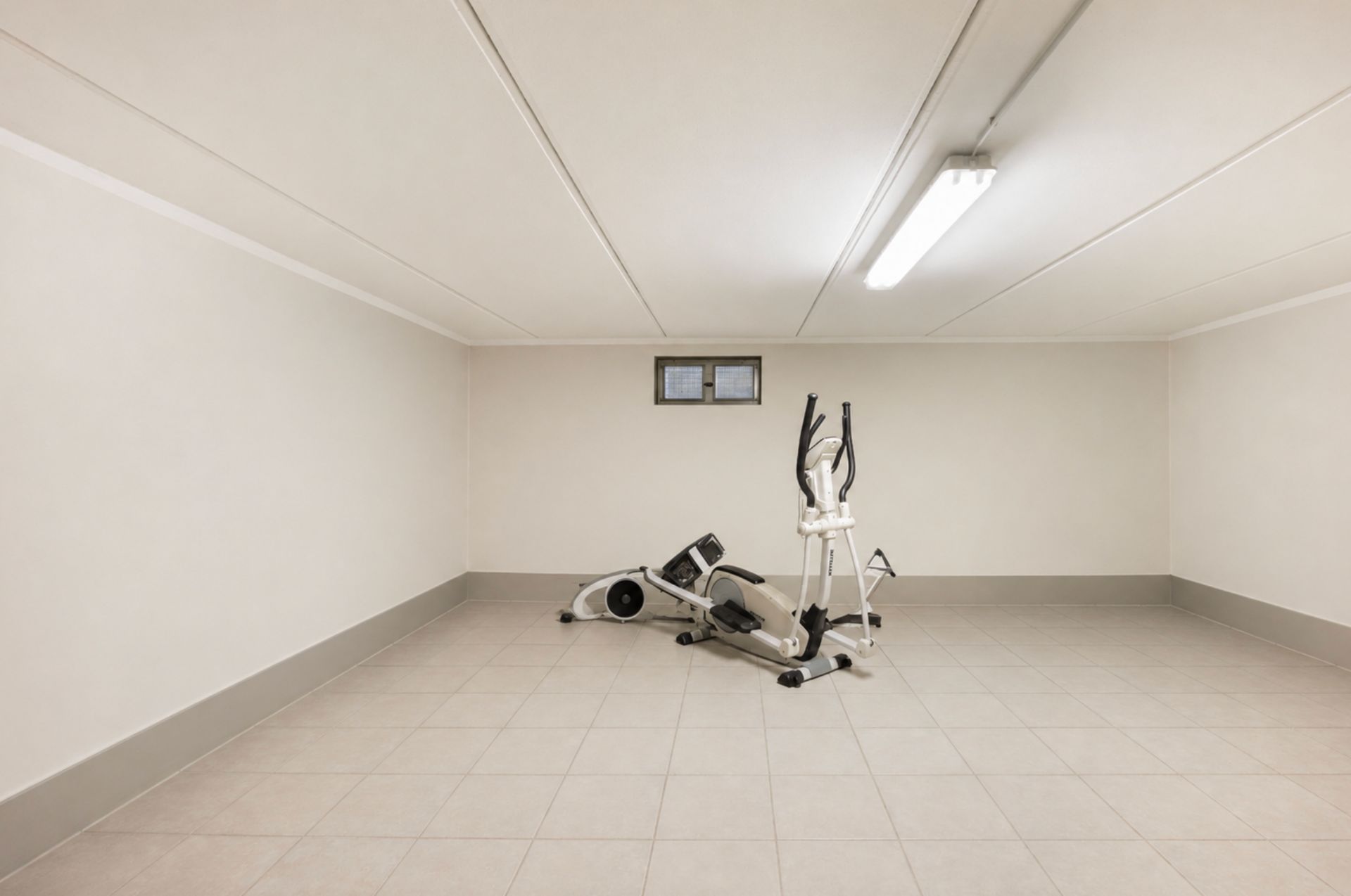 Leerer Kellerraum mit einem einzelnen Fitnessgerät und kleinem Fenster an der Wand.