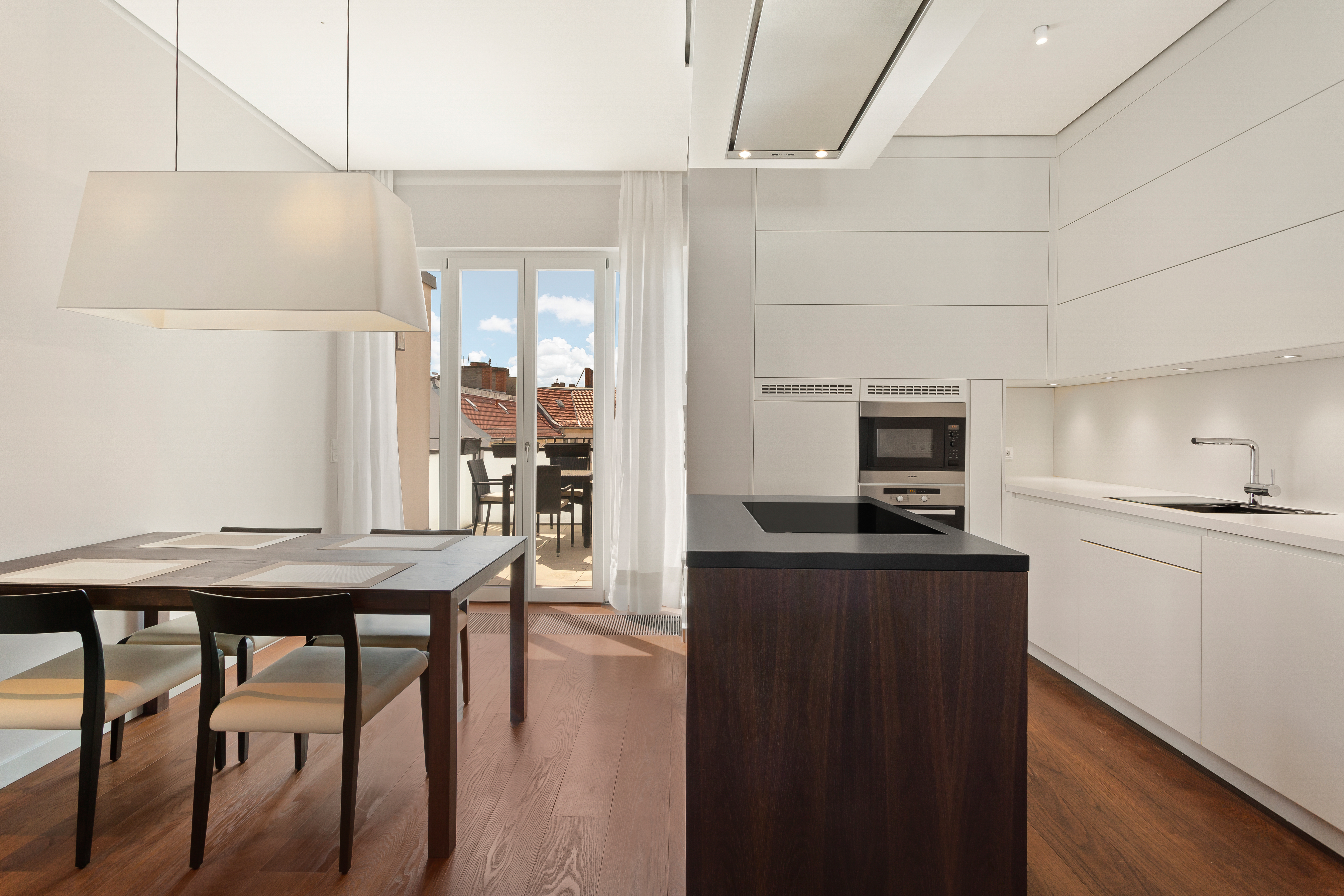 Moderne Küche mit weißer Einrichtung, Holzboden, Esstisch und Zugang zum Balkon.