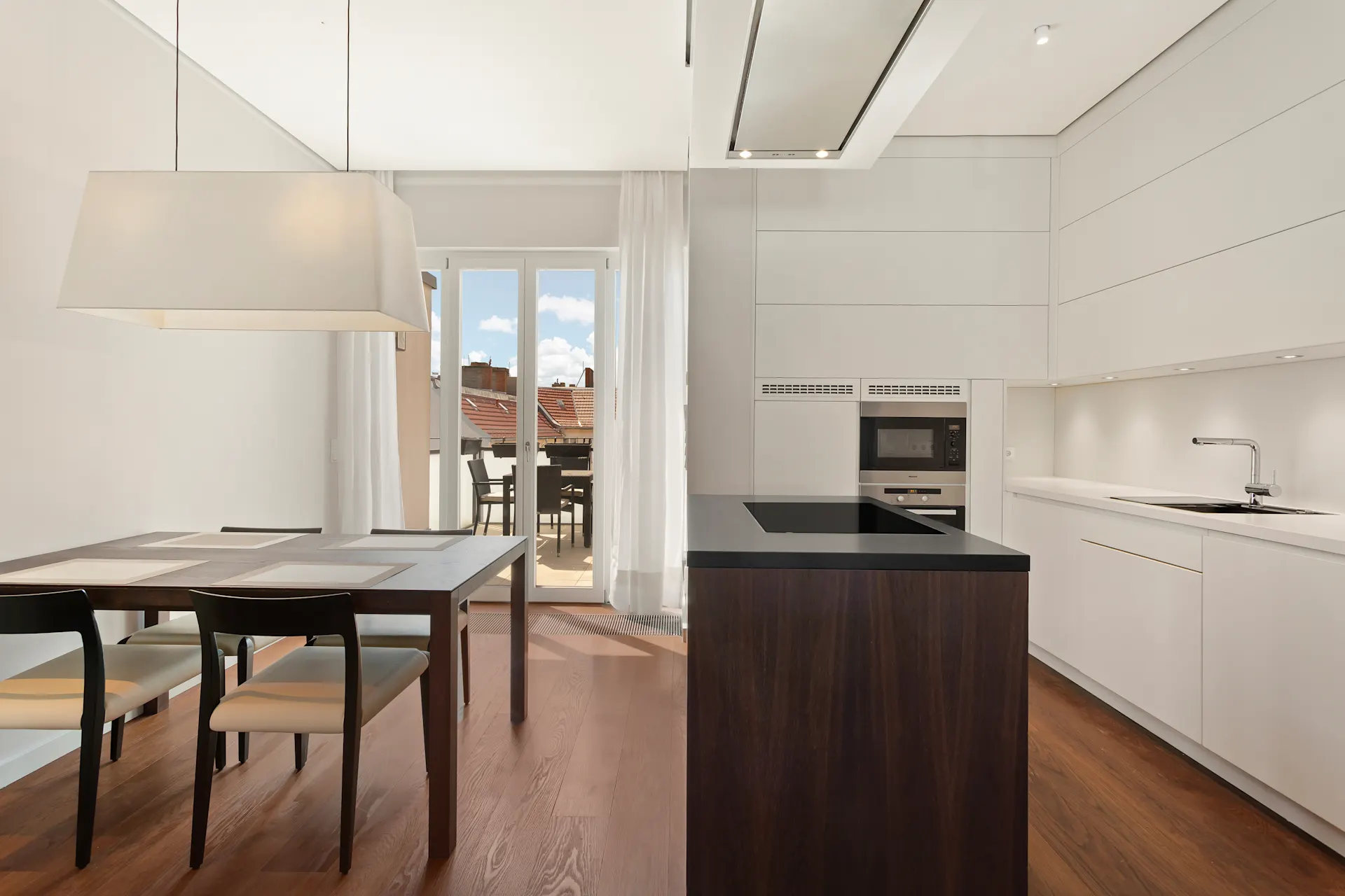 Moderne Küche mit weißer Einrichtung, Holzboden, Esstisch und Zugang zum Balkon.