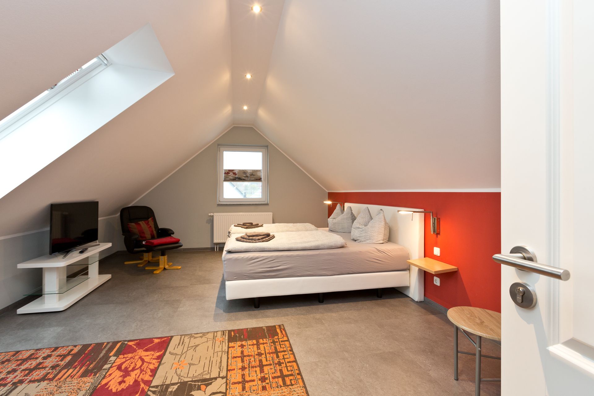Gemütliches Schlafzimmer im Dachgeschoss mit Doppelbett, Fernseher und Dachfenster.
