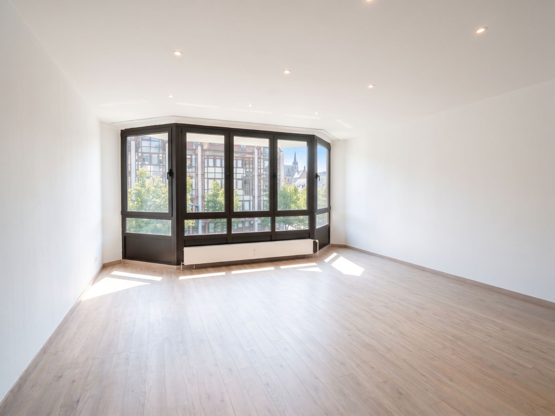 Helles, leeres Zimmer mit großem Fenster und Holzfußboden.