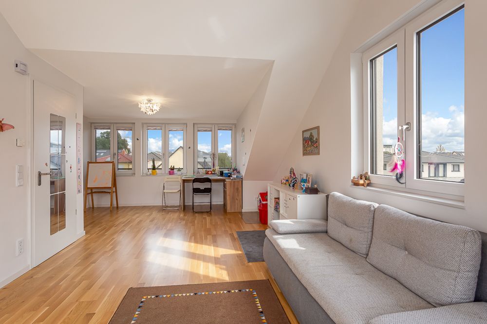 Helles Wohnzimmer mit grauem Sofa, Schreibtisch, Holzfußboden und großen Fenstern.