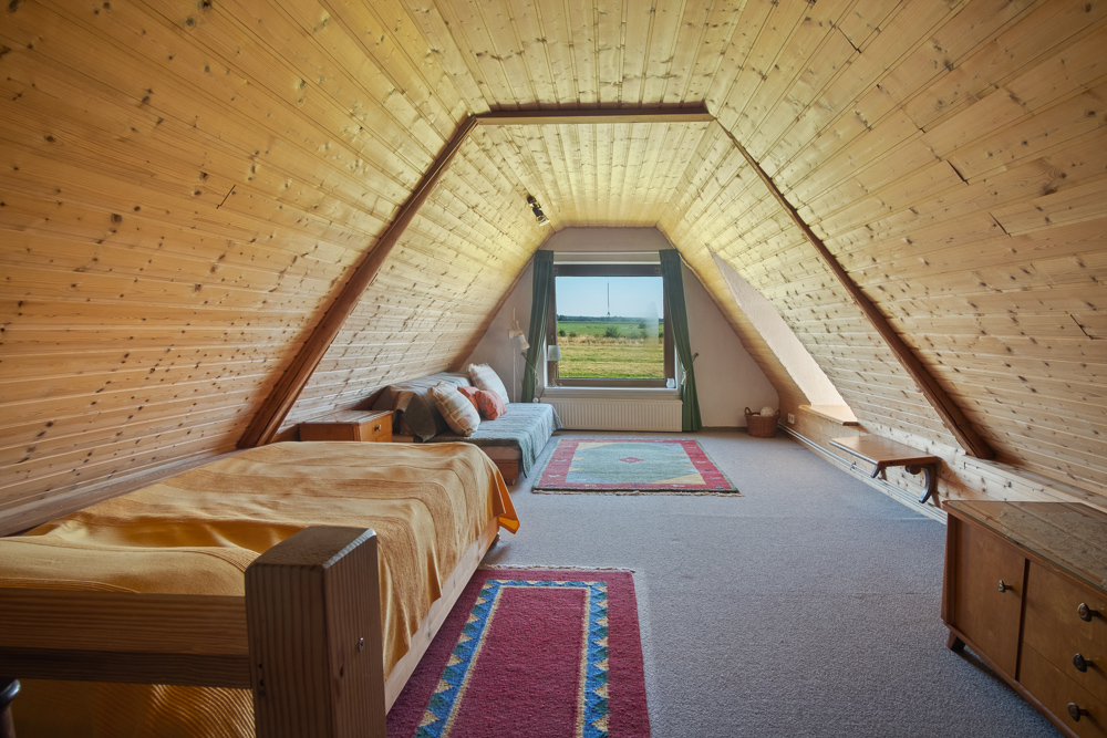 Dachzimmer mit Holzverkleidung, Bett, Sofa und großem Fenster mit Blick ins Grüne.