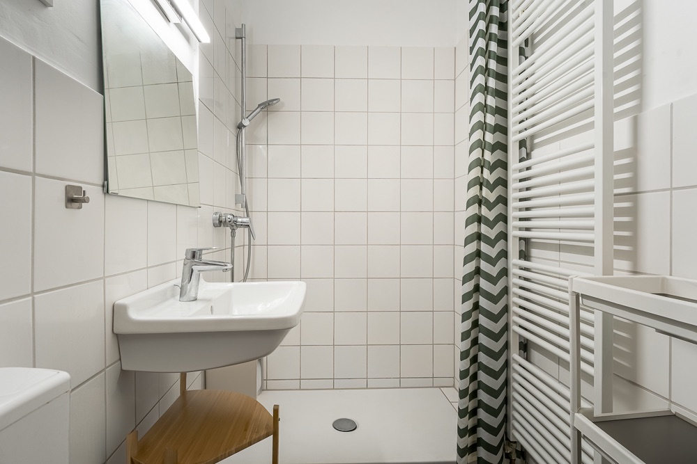 Modernes Badezimmer mit Dusche, Waschbecken, Spiegel und Handtuchheizkörper.