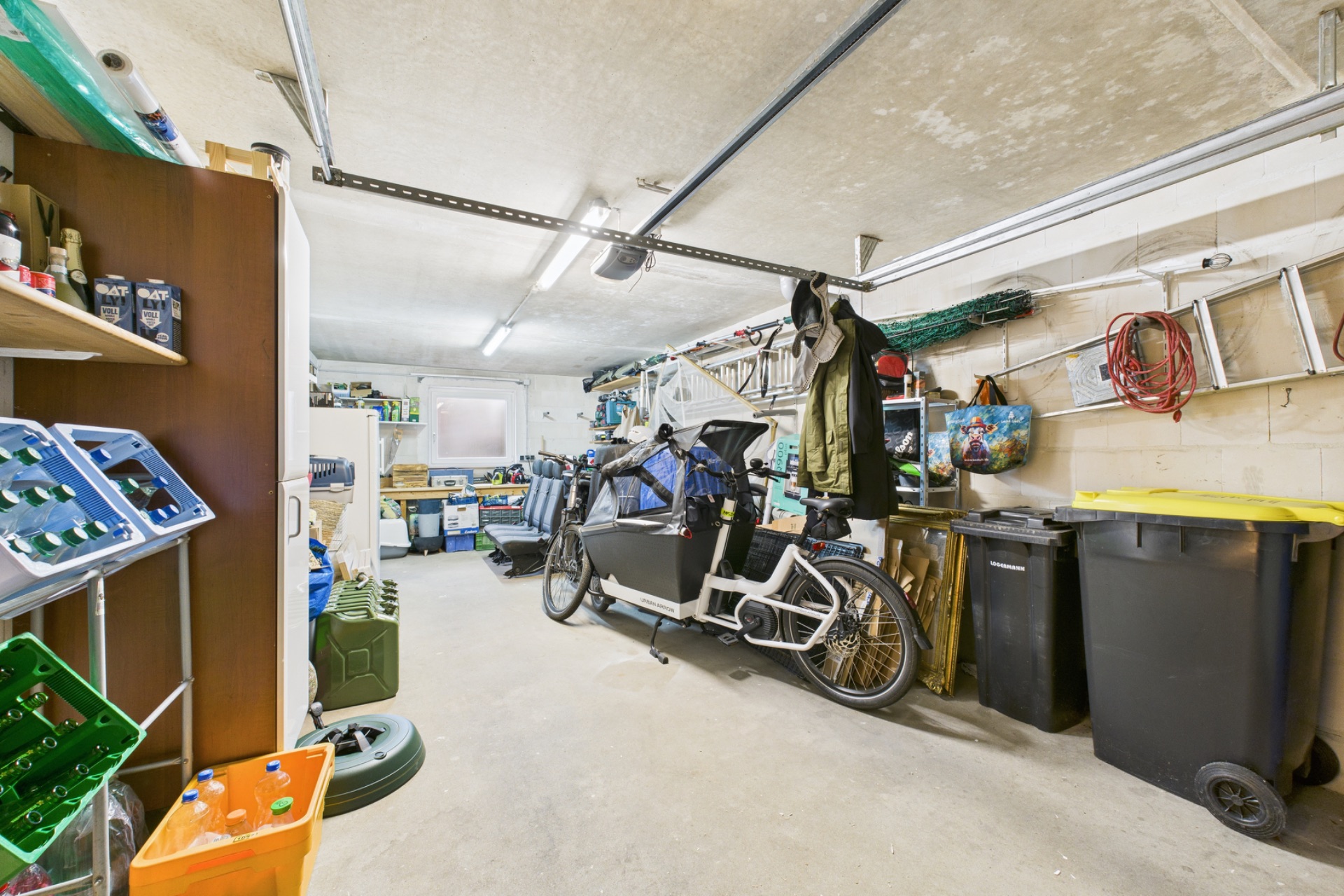 Garage mit Lastenfahrrad, Mülltonnen, Werkzeug, Regalen und Leitern an der Wand.