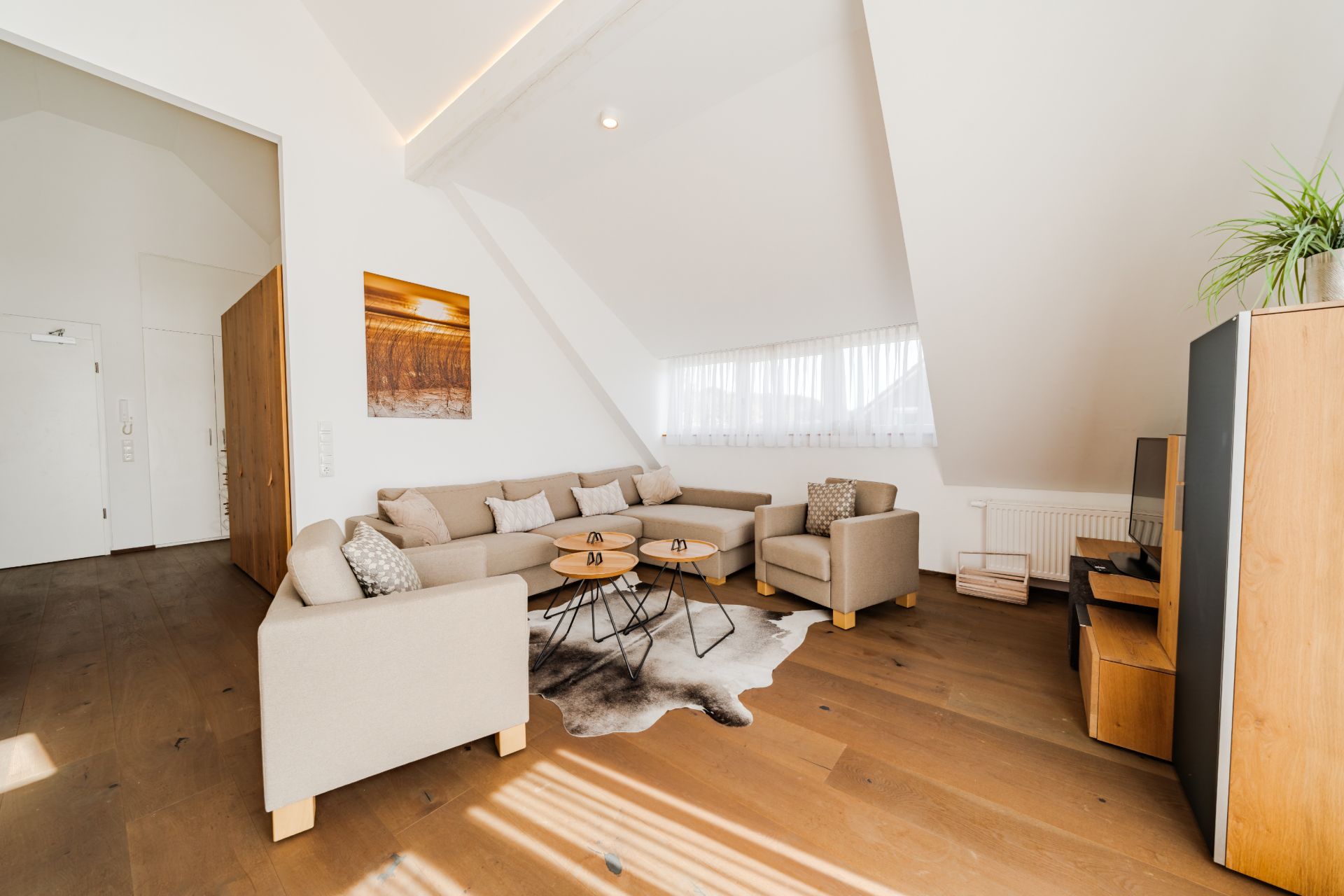 Helles Wohnzimmer mit Sofa, Sesseln, Couchtischen und Fernseher unter einer Dachschräge.