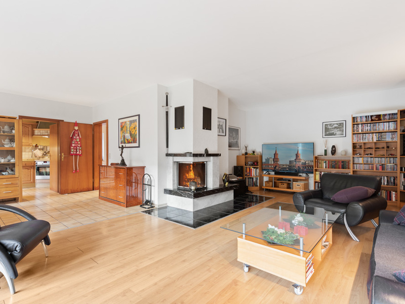 Helles Wohnzimmer mit Kamin, Holzboden, Sofa, Glastisch und Bücherregalen.