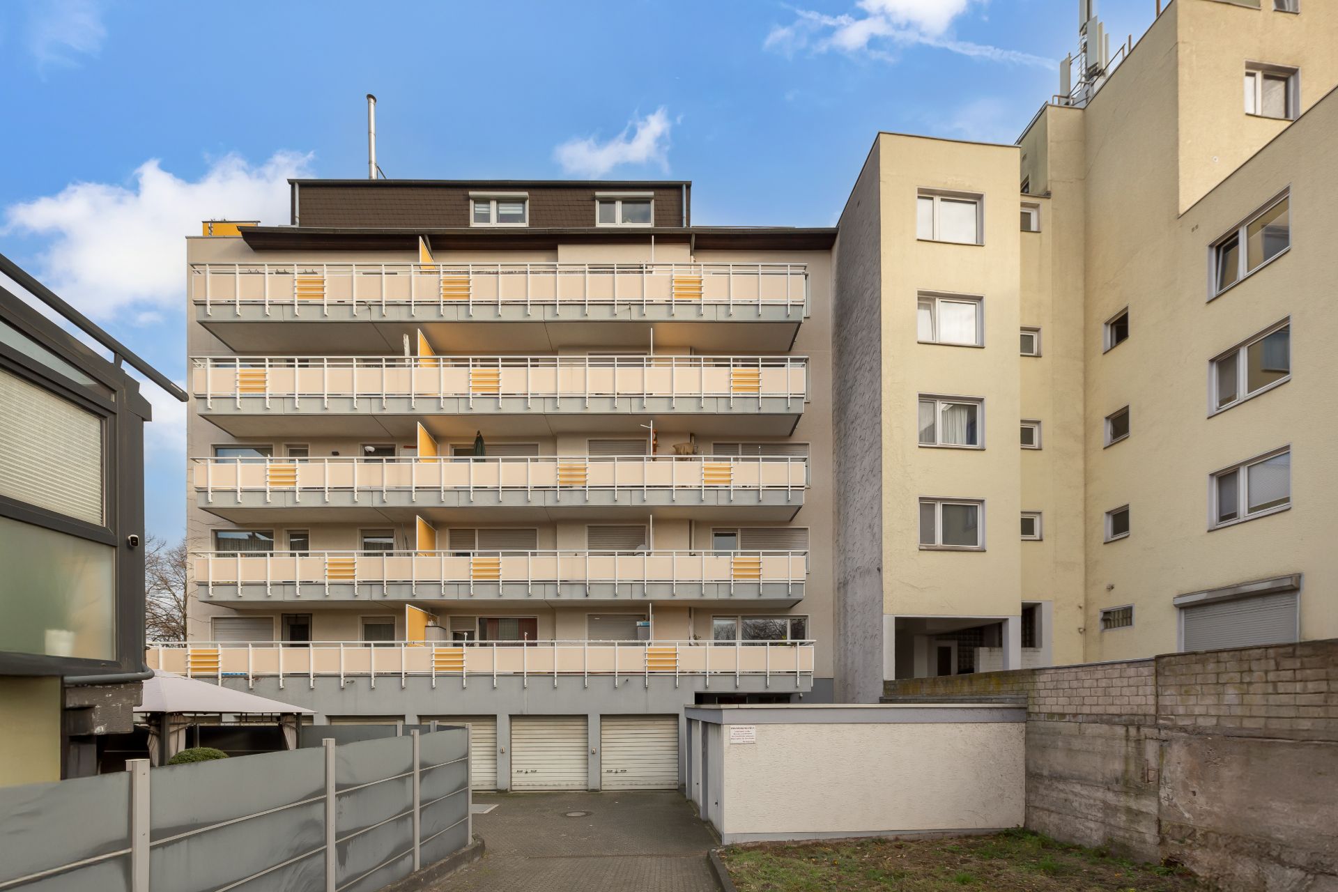 Mehrstöckiges Wohngebäude mit Balkonen und Garagen im Erdgeschoss.