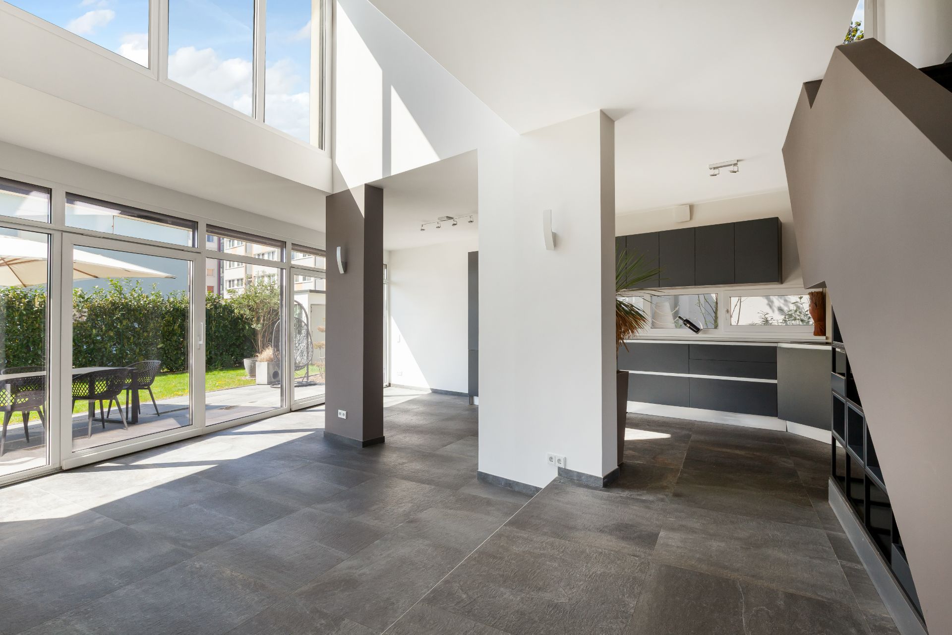 Moderner, offener Wohnraum mit großen Fenstern, Blick auf Küche und Zugang zur Terrasse mit Garten.
