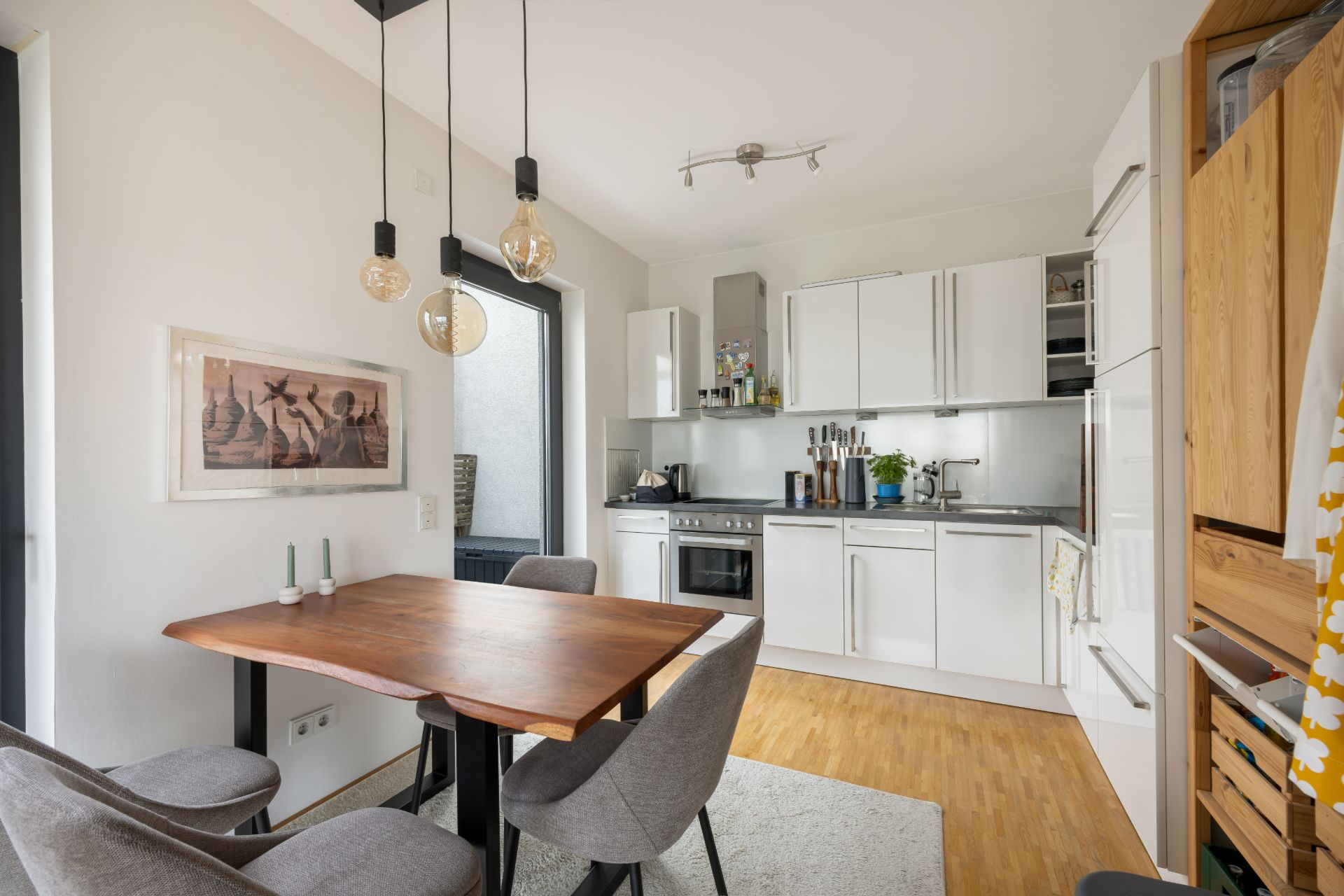 Moderne Küche mit Esstisch, vier Stühlen und weißen Schränken auf Holzfußboden.