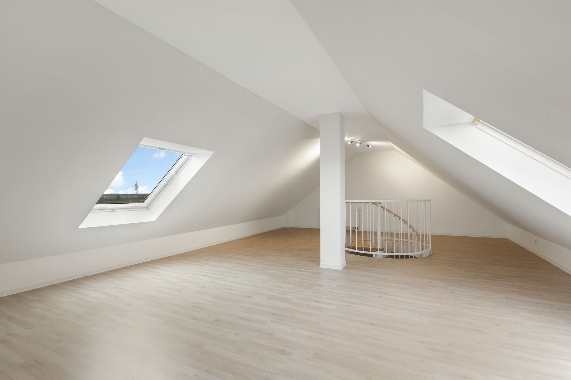 Heller Dachbodenraum mit zwei Dachfenstern, Holzfußboden und Wendeltreppe.