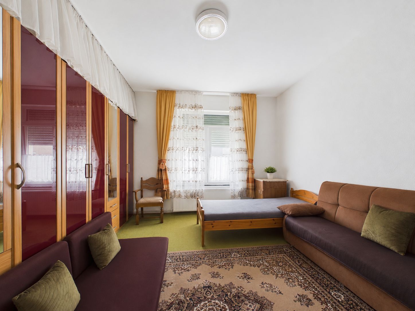 Wohnzimmer mit Sofa, Bett, Schrank und Fenster mit gelben Vorhängen.